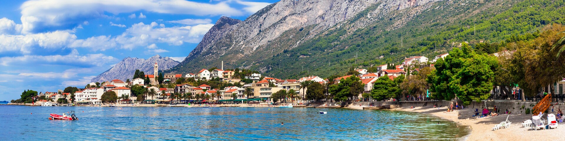 A coastal town with a mountain backdrop, a beach, and a boat in the water.