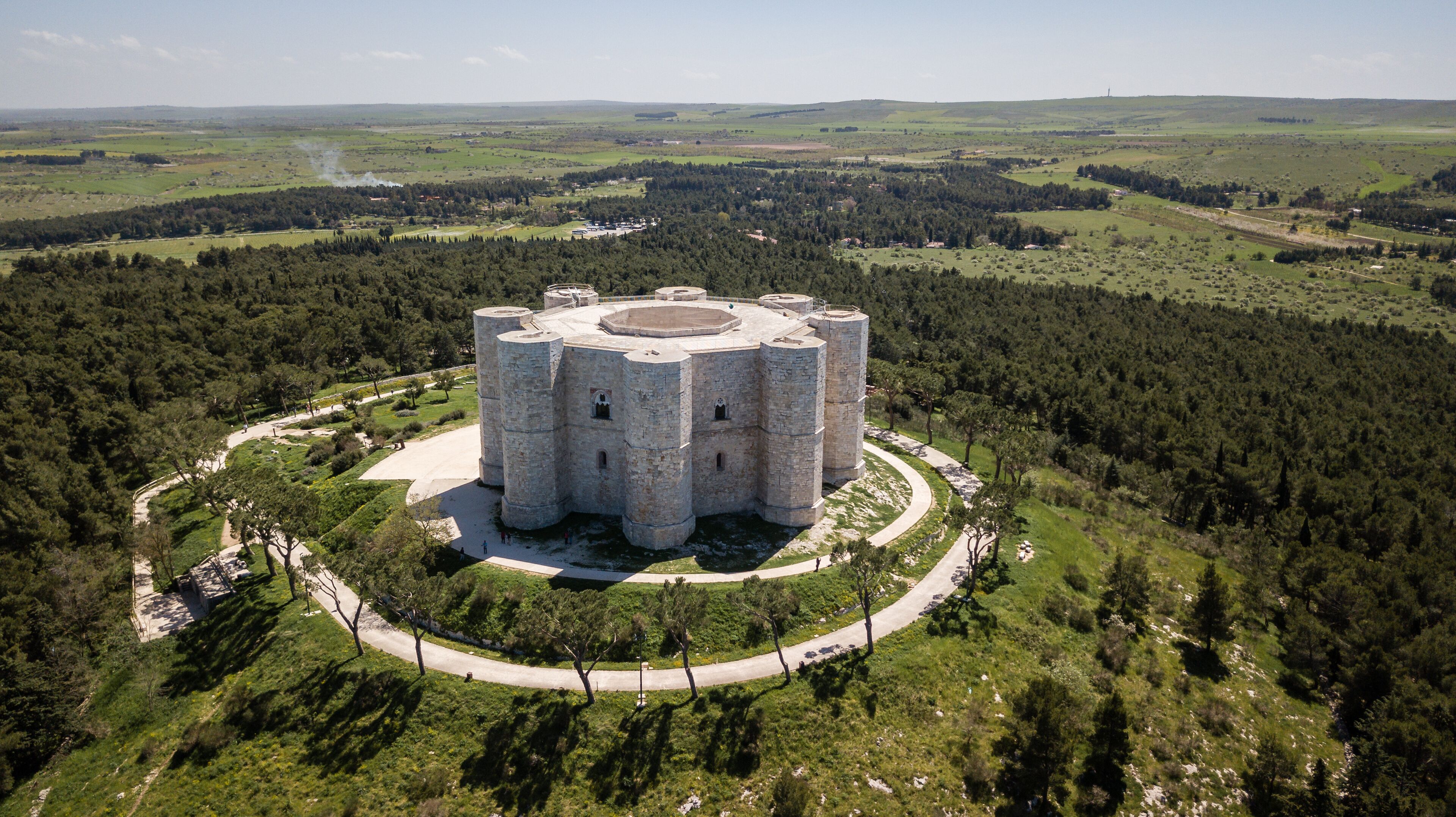 A large stone castle surrounded by a forested area with a clear sky.