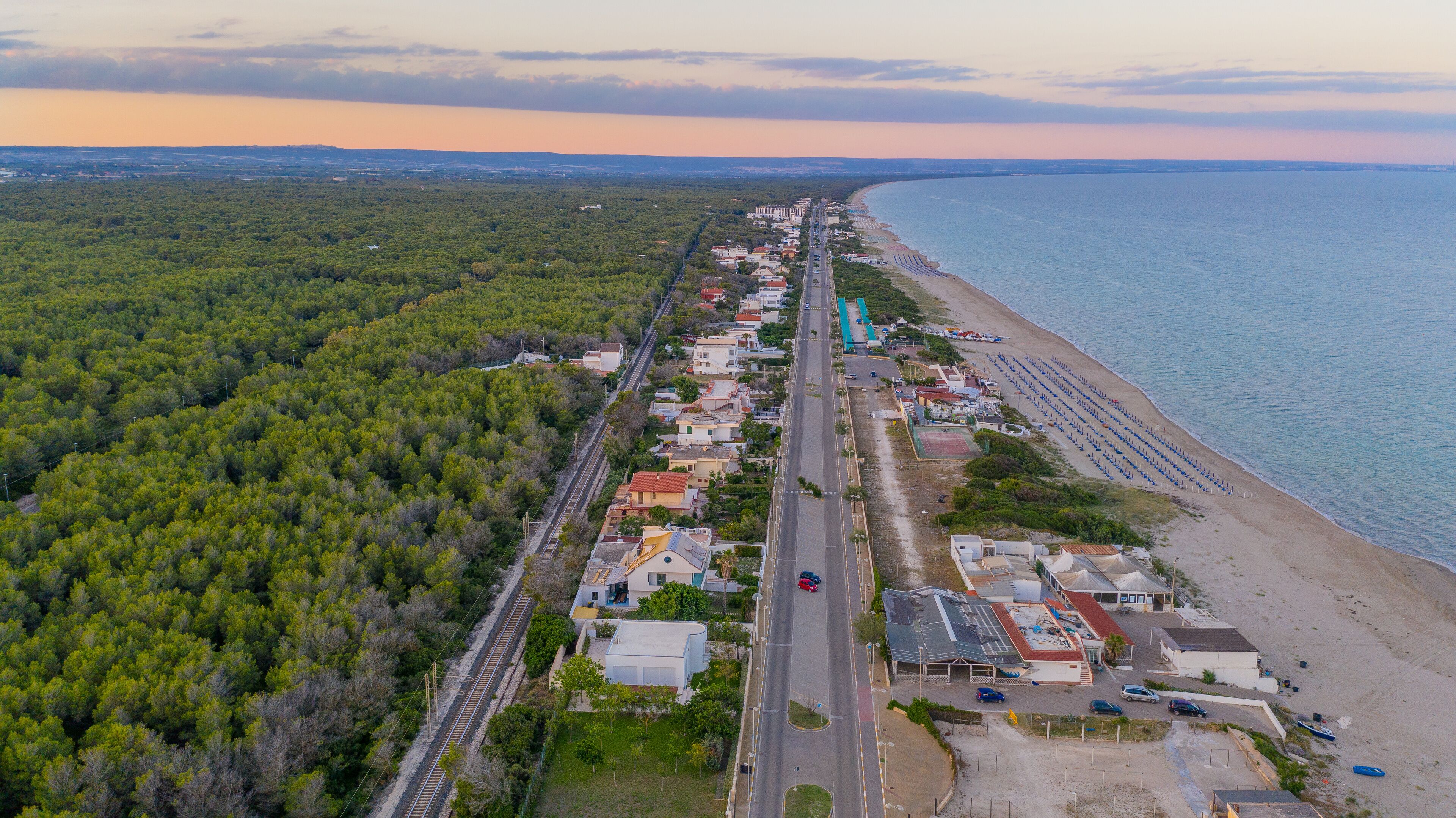 An aerial view of a coastal town with a beach, dense forest, and a railway line.