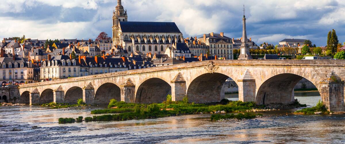 A stone bridge with arches over a river, a historic building with a tower, and a monument in the background.