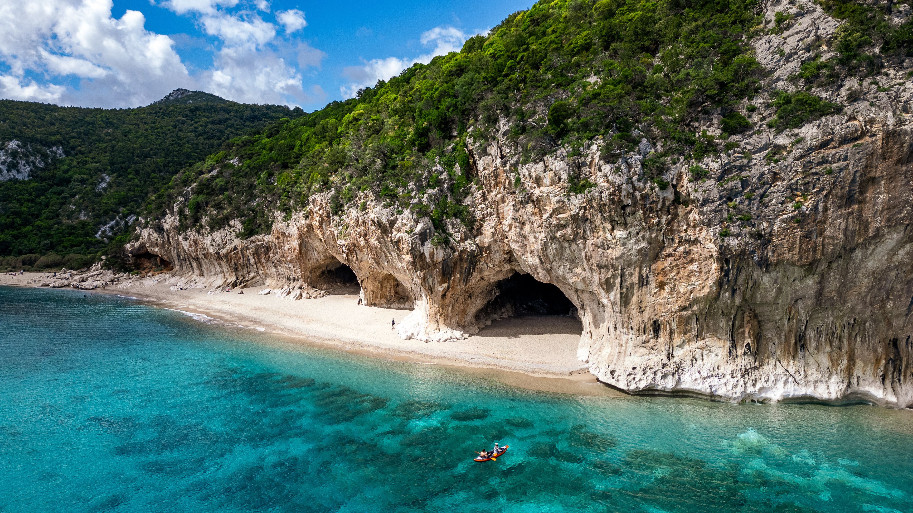 Un paisaje costero con un acantilado rocoso, una playa y aguas turquesas cristalinas.