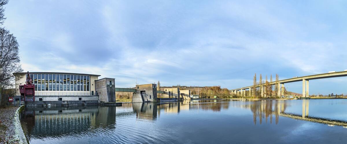 A calm river with a bridge and industrial buildings.