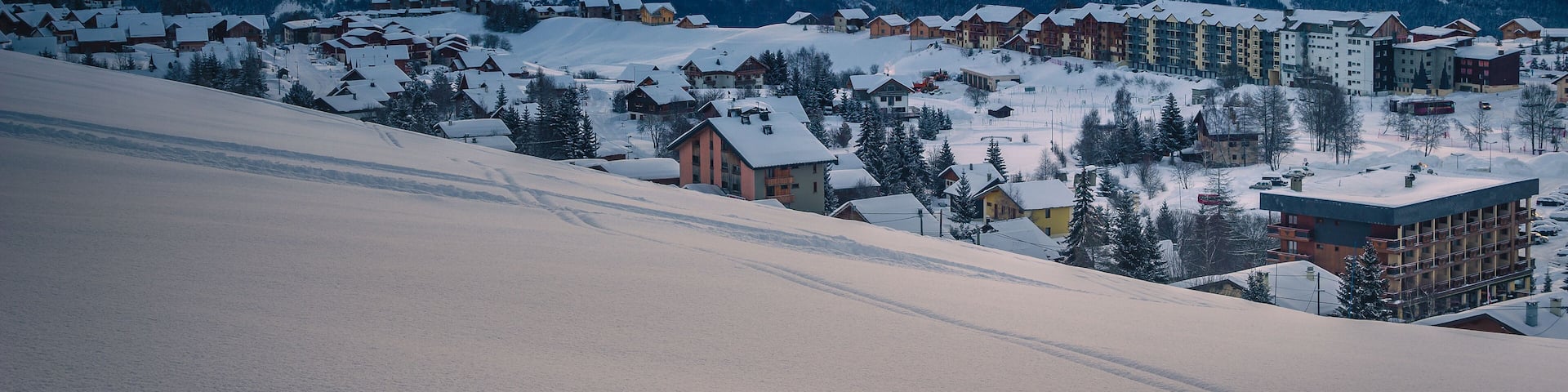 A snow-covered mountain range with a village at the base during sunset.