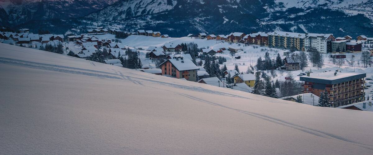 A snow-covered mountain range with a village at the base during sunset.
