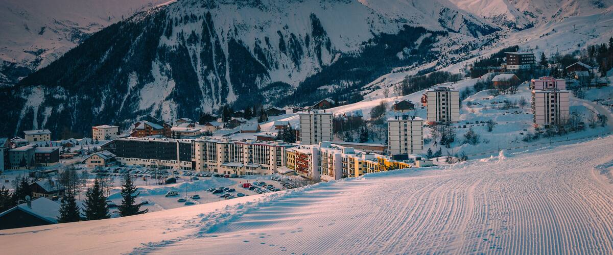 A snow-covered mountain range with a town at the base, featuring buildings and a ski slope.