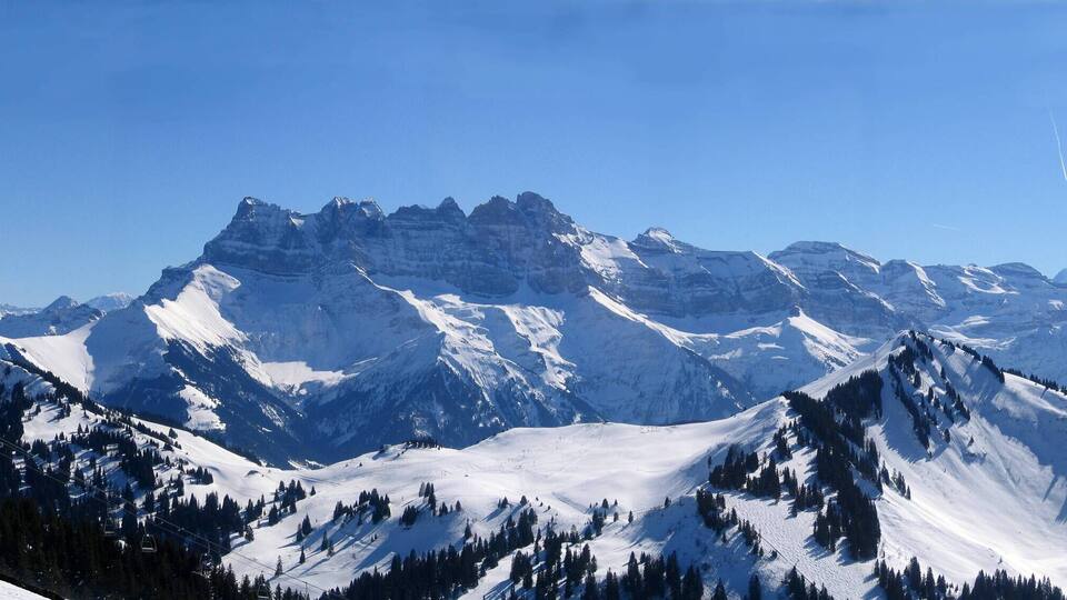 Snow-covered mountain peaks, a ski lift, and a clear blue sky.