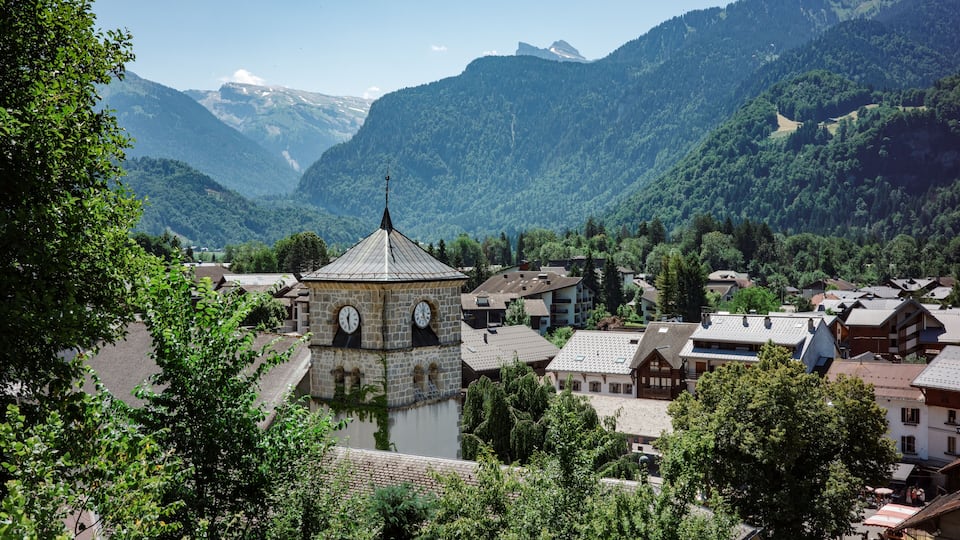 A town with a clock tower, surrounded by mountains and a river.