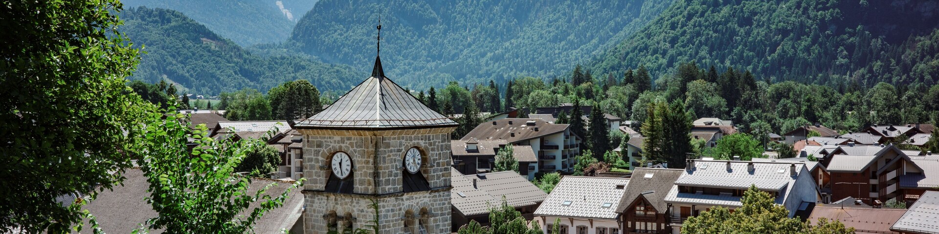 A town with a clock tower, surrounded by mountains and a river.