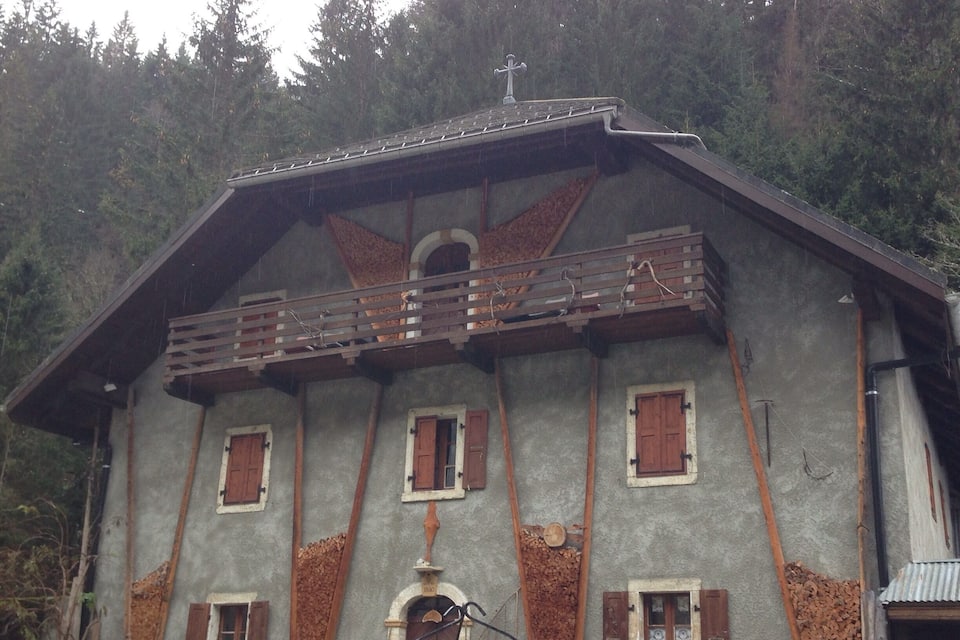 A rustic wooden house with a sloped roof, wooden shutters, and a chimney.