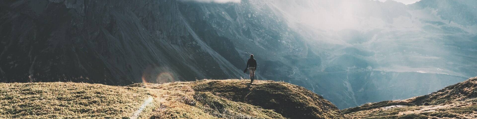 A hiker on a mountain ridge with mist-covered peaks and a valley below.