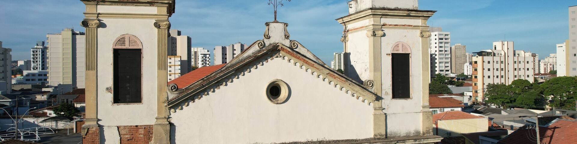A church with two towers and a cross on the roof, surrounded by urban buildings.