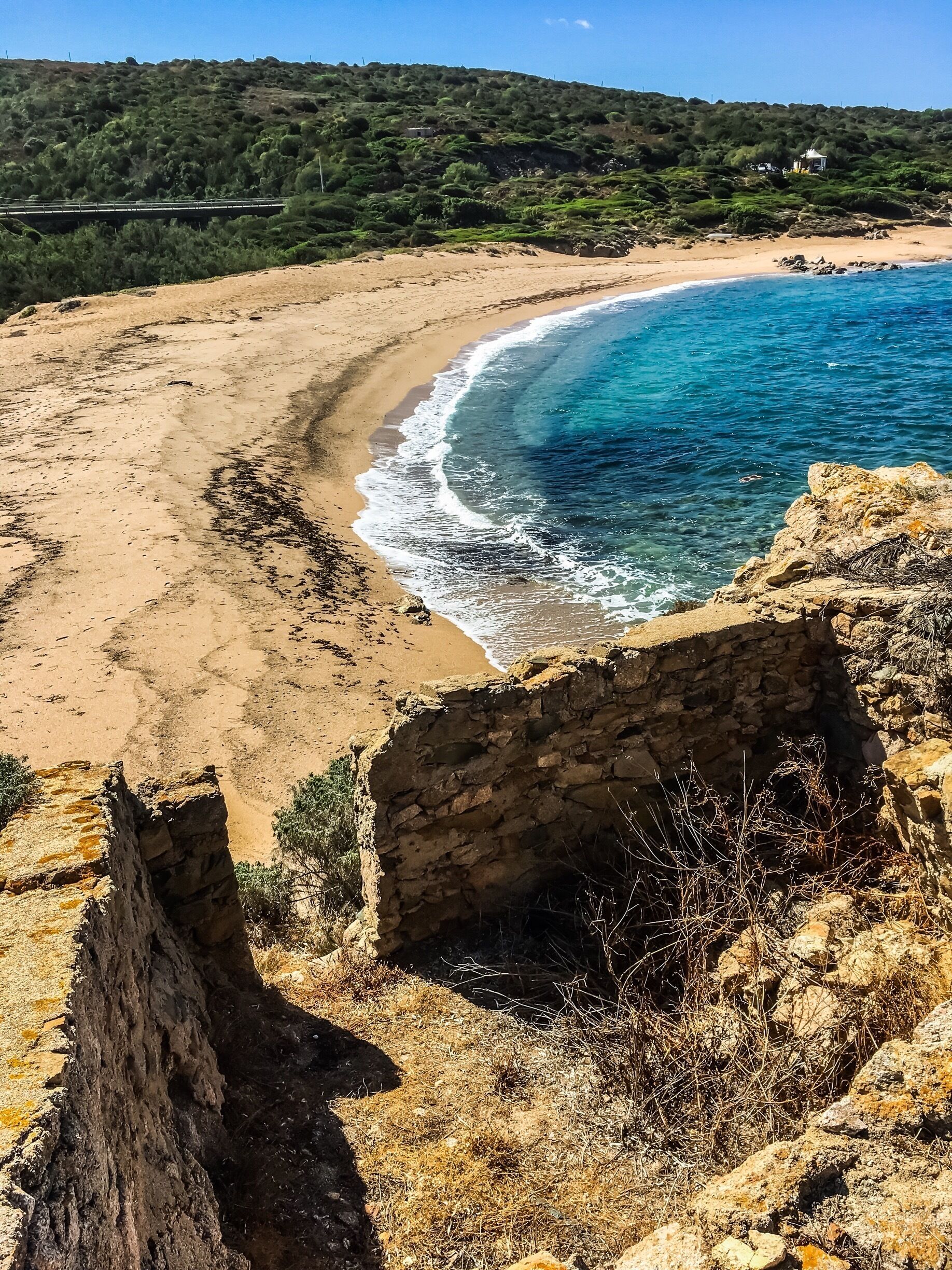 A coastal landscape with a sandy beach, clear blue waters, and rocky cliffs.