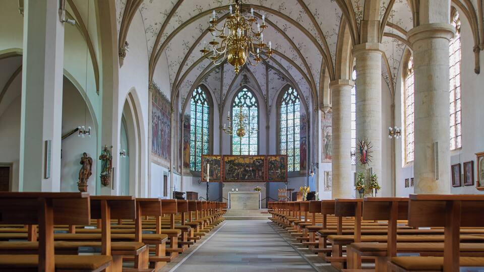 An interior of a church with wooden pews, a central altar, stained glass windows, and a chandelier.