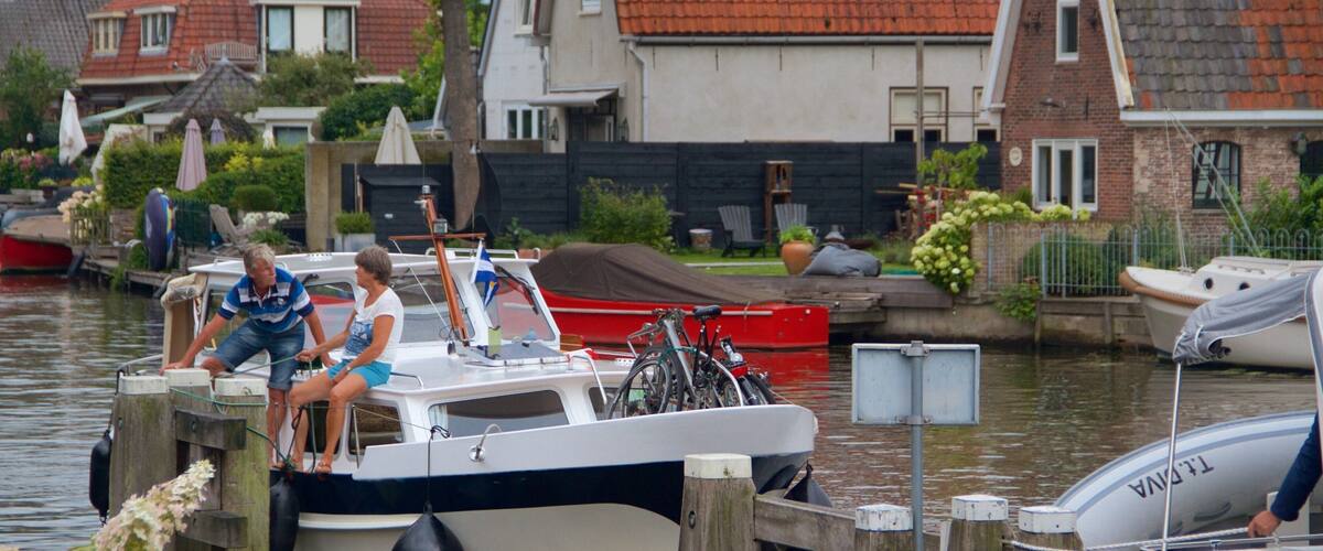 A canal with boats docked, a red boat in the foreground, and houses with red-tiled roofs in the background.