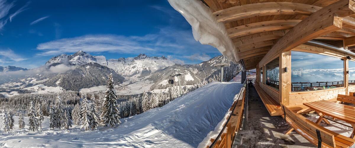 A wooden cabin with benches overlooking a snowy mountain landscape.