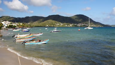 A beach with small boats anchored near the shore, a clear blue sea, and a mountainous backdrop.