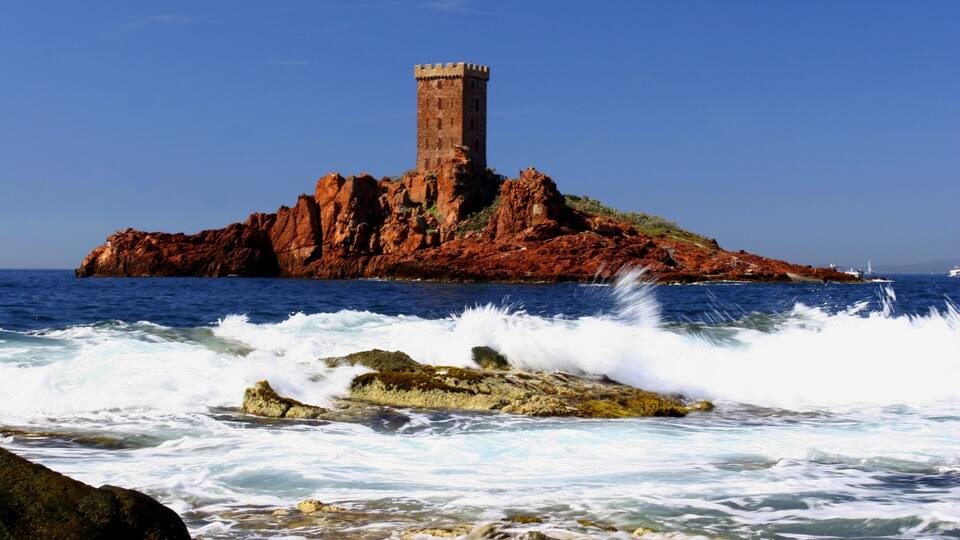 A coastal landscape with a prominent red rock formation and a tower on top.