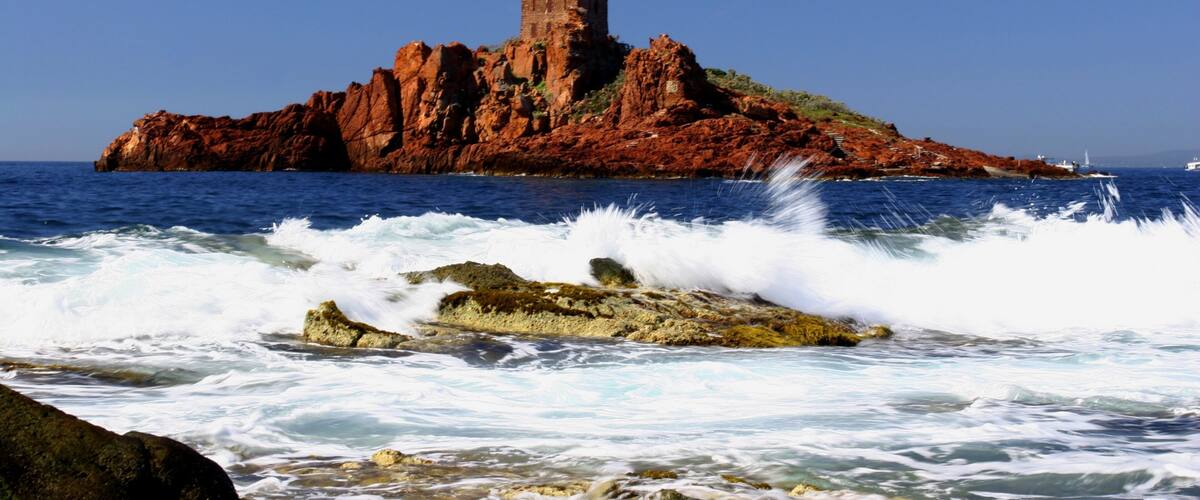 A coastal landscape with a prominent red rock formation and a tower on top.