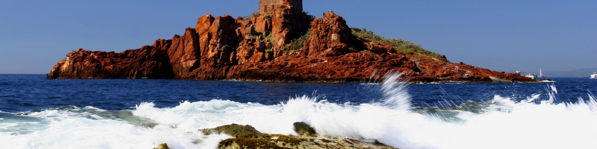 A coastal landscape with a prominent red rock formation and a tower on top.