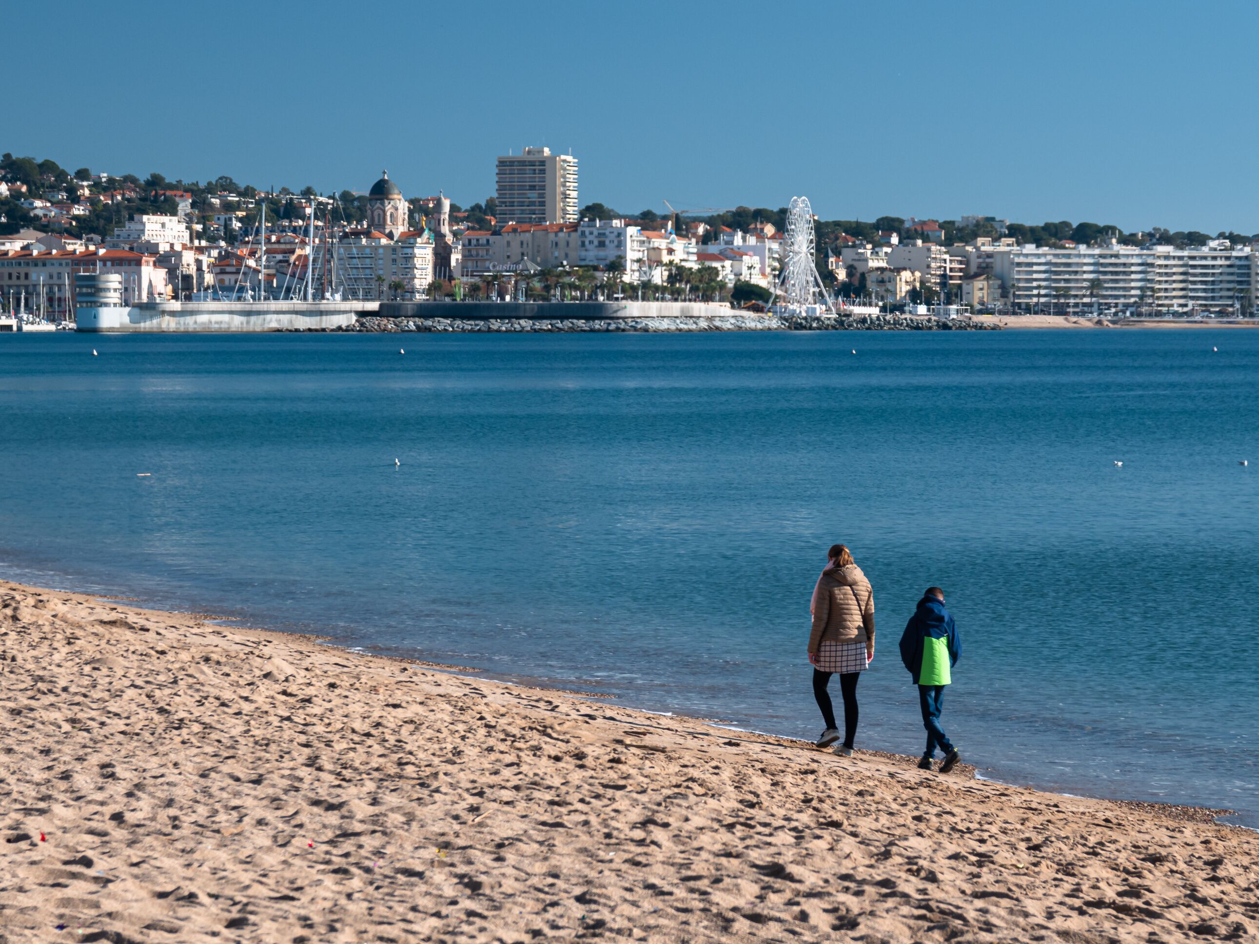 FREJUS, FRANCE - JANUARY 1, 2020: Mother and her son walking in winter on the mediterranean beach of Frejus with a wonderful view to Saint Raphael.