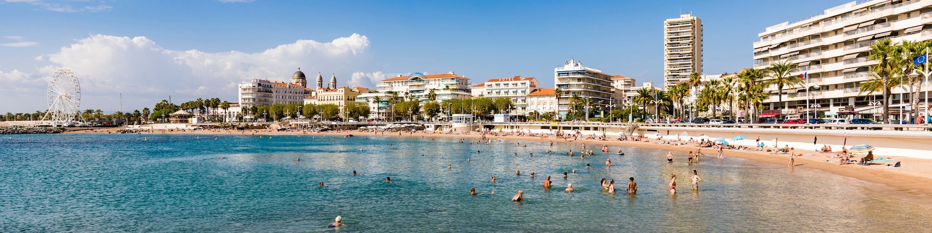 Un paisaje urbano costero con mar azul cristalino, una playa arenosa y diversos edificios, incluyendo hoteles y una estructura moderna alta.