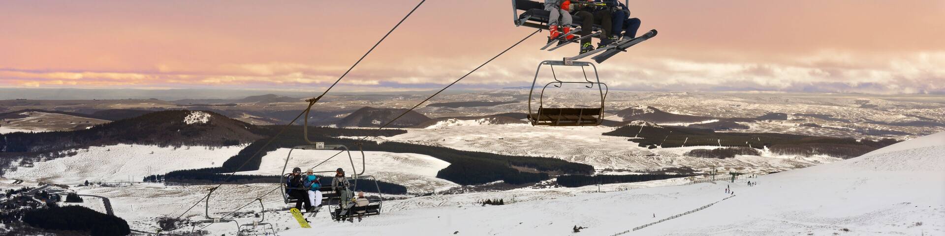 A ski lift with passengers, a snowy mountain landscape, and a sunset sky.