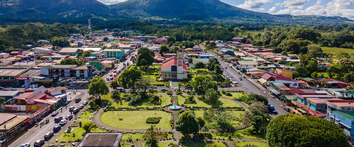 A town with colorful buildings, a central park, and a volcano in the background.