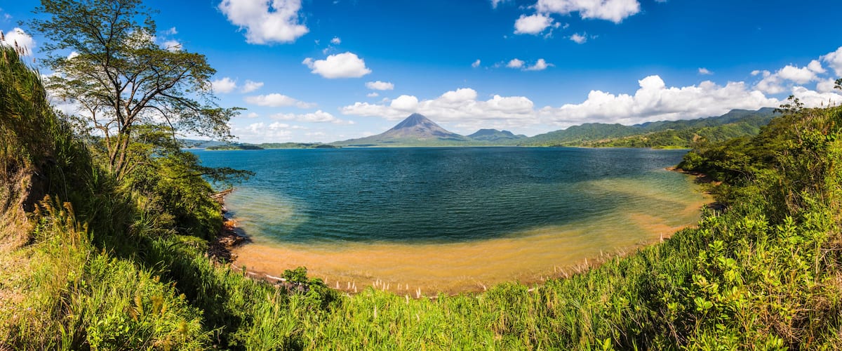 A coastal landscape with a clear view of a mountain in the distance, surrounded by lush greenery and a calm sea.