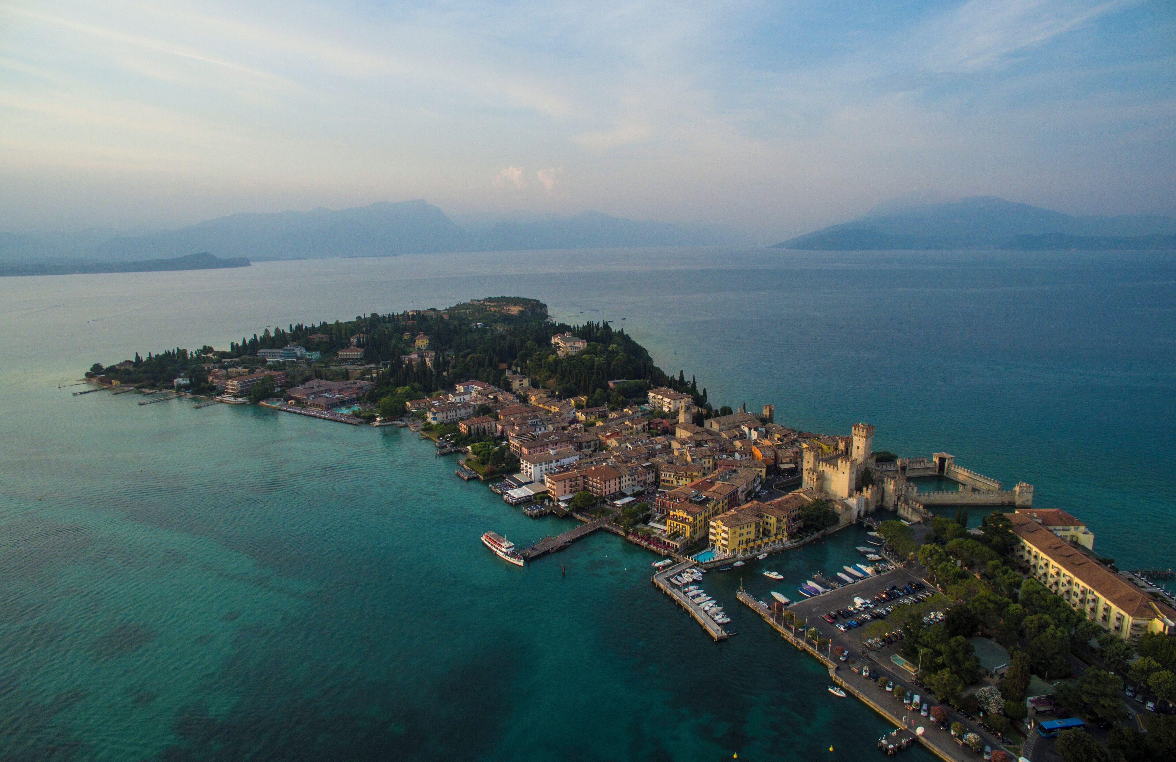 An aerial view of a coastal town with a prominent castle, clear turquoise waters, and a small island with buildings.