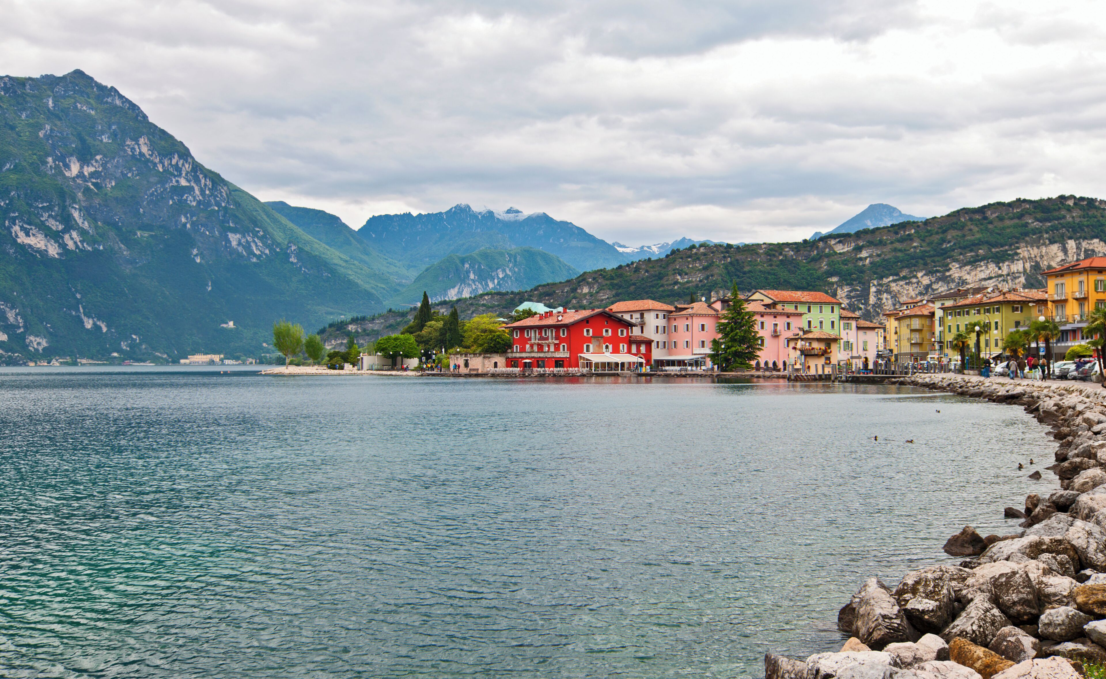 A lake with colorful buildings along the shore, mountains in the background, and a rocky shoreline.