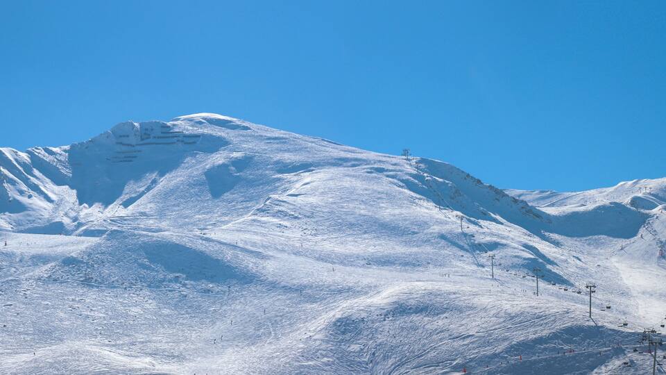 A snow-covered mountain with ski slopes and a clear blue sky.
