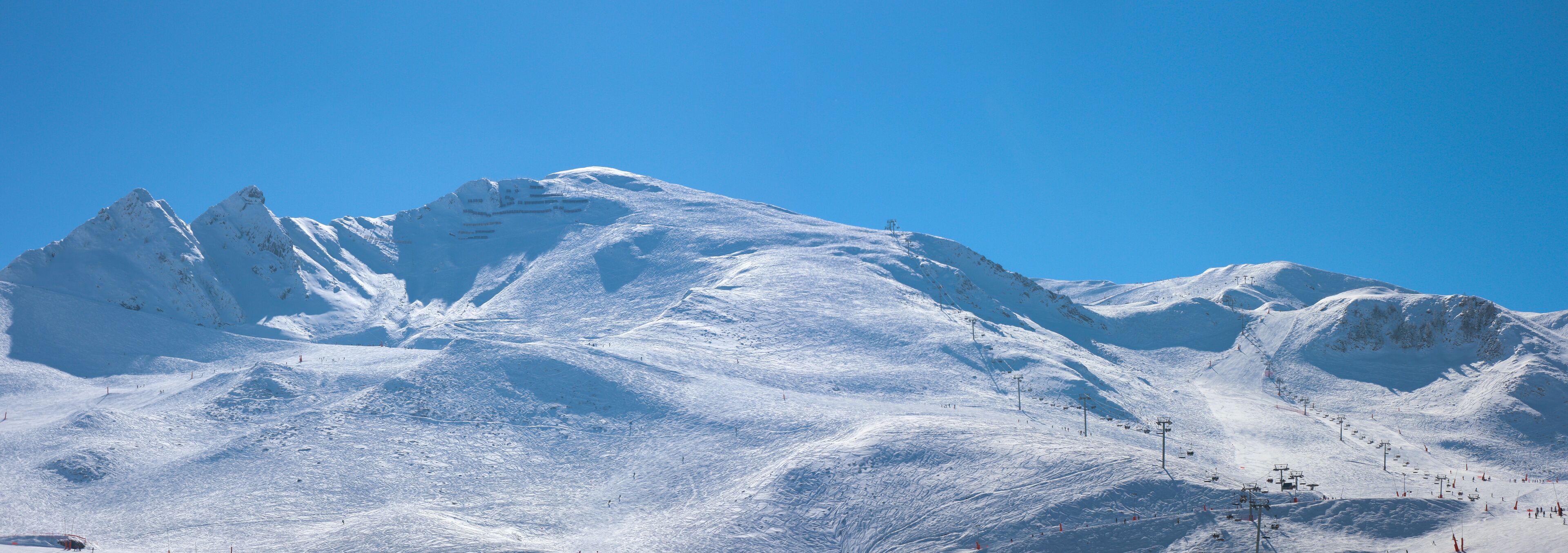A snow-covered mountain with ski slopes and a clear blue sky.