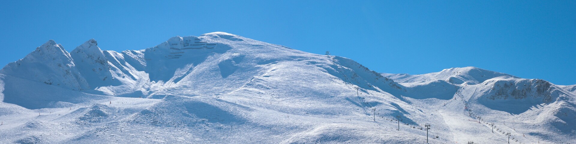 A snow-covered mountain with ski slopes and a clear blue sky.