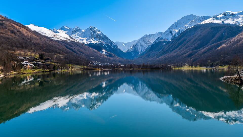 A serene lake surrounded by snow-capped mountains, with reflections of the peaks in the calm water.