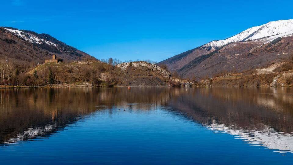 A tranquil lake surrounded by mountains with a castle-like structure on a hill.