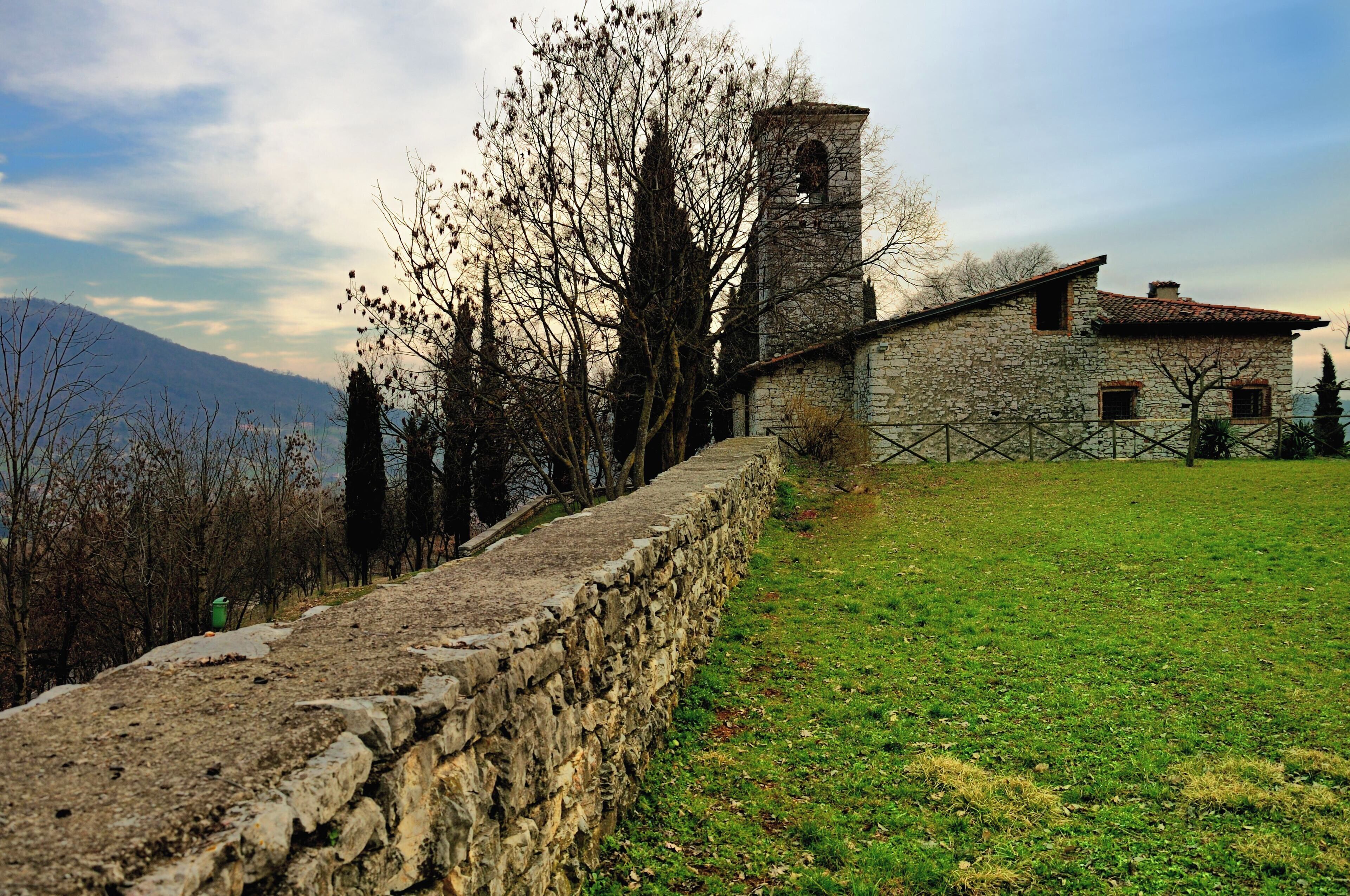 A stone wall, a stone building with a bell tower, and a grassy field with trees.