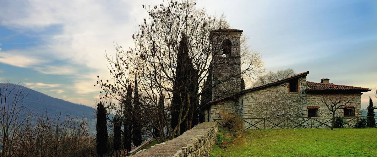 A stone wall, a stone building with a bell tower, and a grassy field with trees.