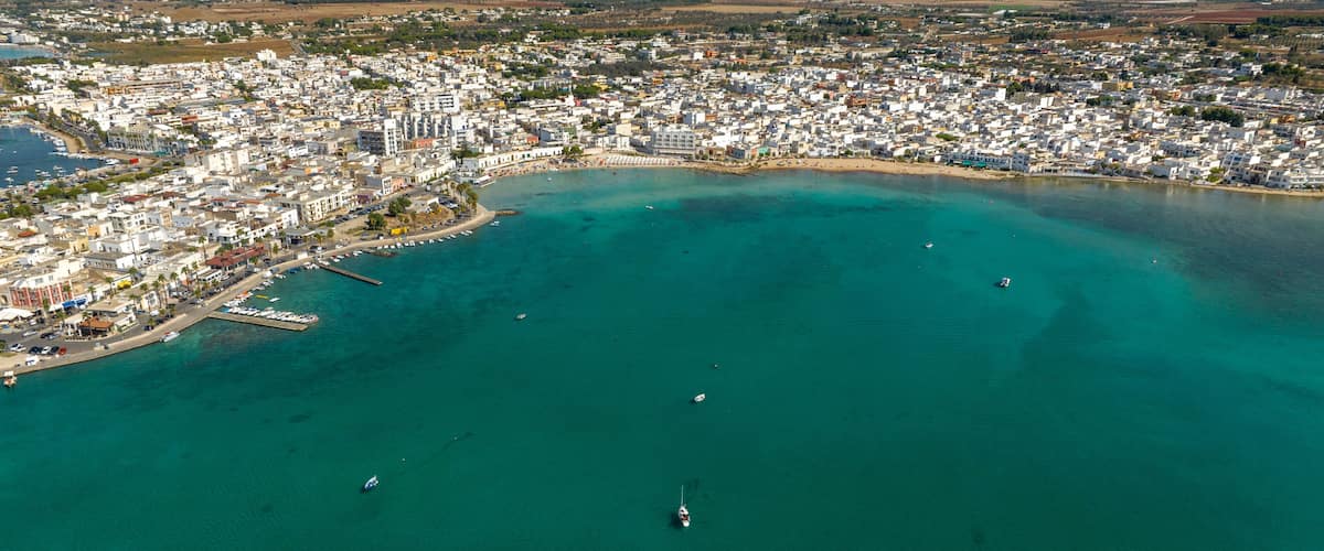A coastal cityscape with a marina, clear turquoise waters, and a densely built urban area.