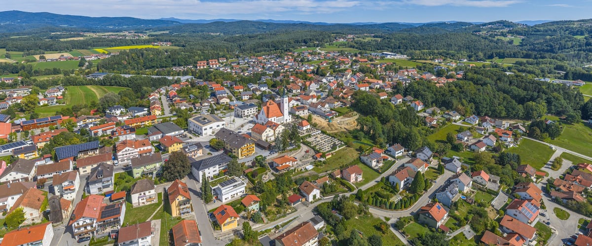 A town with red-roofed houses, a church, and surrounding green hills.