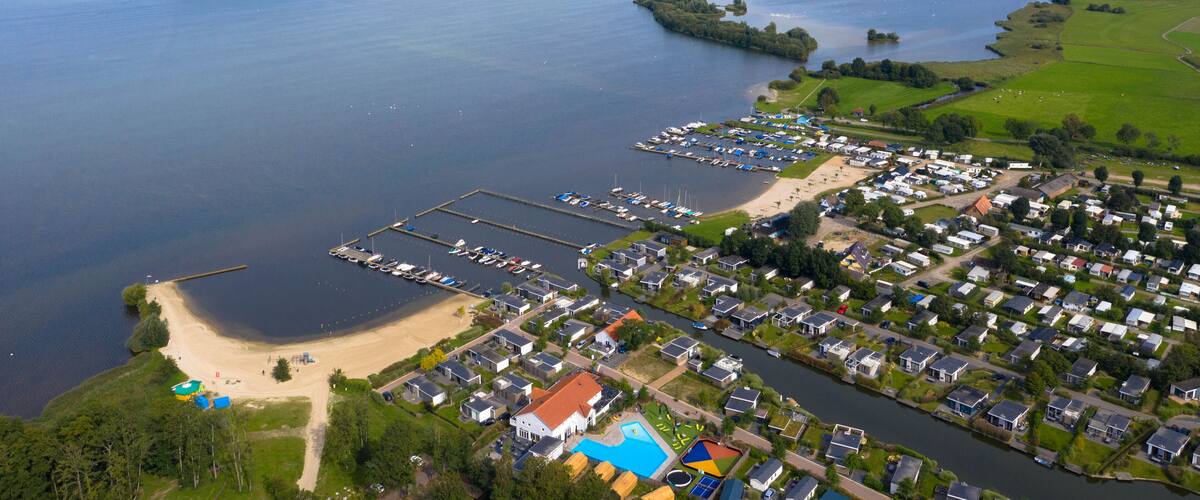An aerial view of a lakeside residential area with boats, a beach, and a marina.