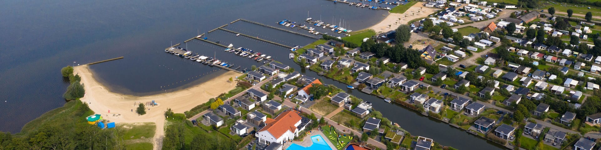 An aerial view of a lakeside residential area with boats, a beach, and a marina.
