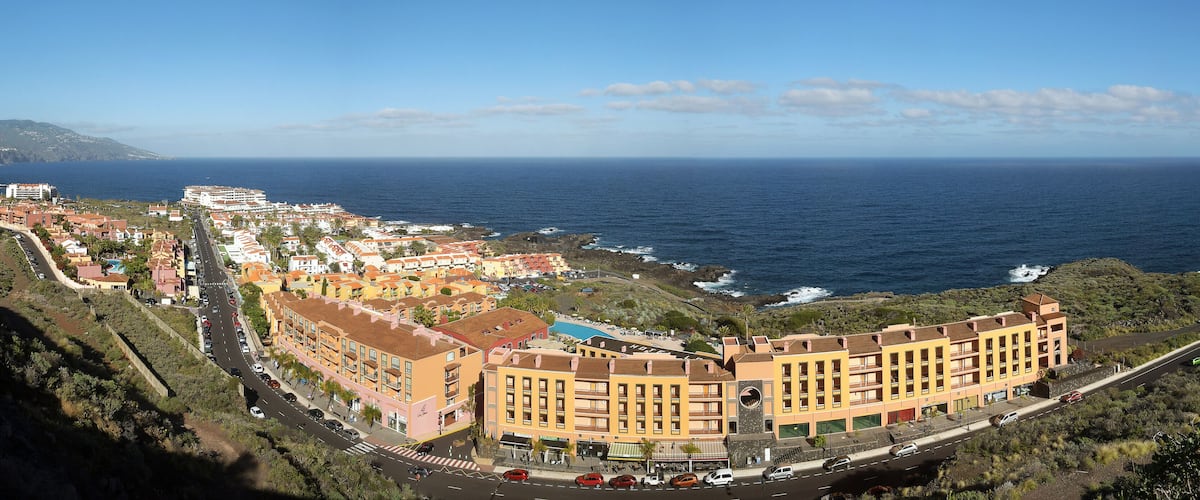 A coastal town with buildings along the sea, a road, and a mountainous backdrop.