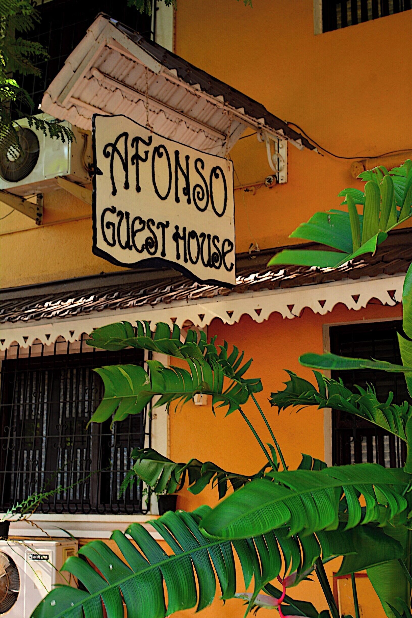 A building with a sign that reads "AFONSO GUEST HOUSE" and large green leaves in front.