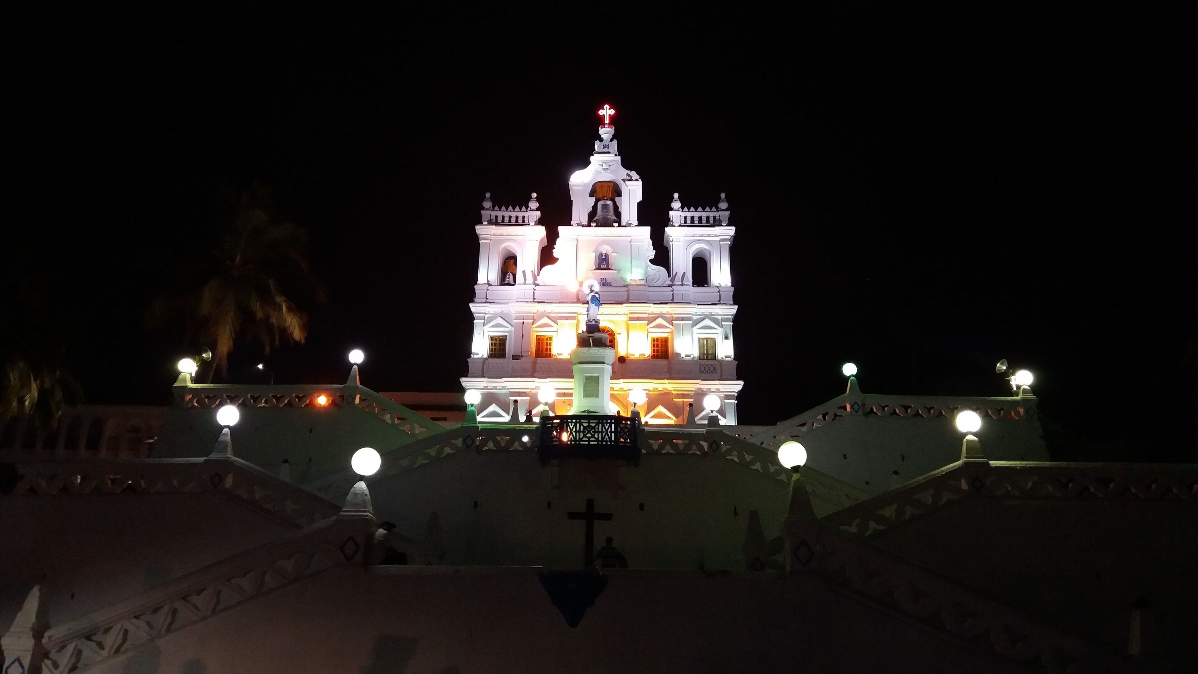 A brightly lit church with a bell tower and a cross on top.