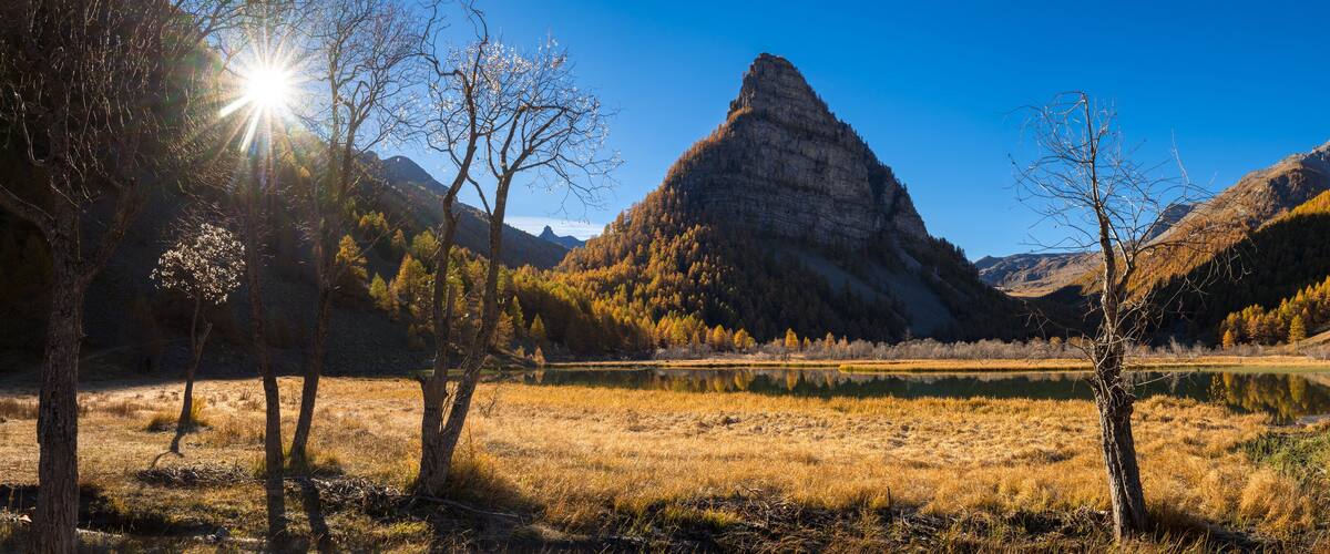 A mountain landscape with a prominent peak, a lake, and autumn-colored trees.