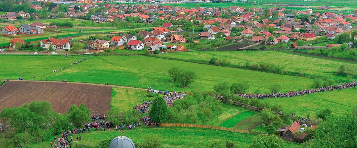 A rural landscape with a large gathering of people, red-roofed houses, and green fields.