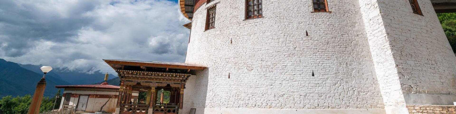 A white stone tower with a curved roof and wooden accents, surrounded by mountains and a clear sky.