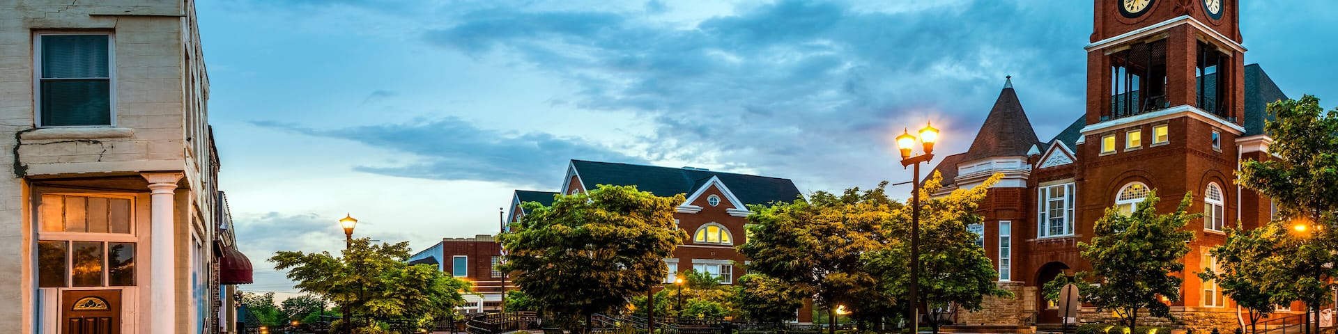 A historic town square with a prominent clock tower, brick buildings, and a well-maintained tree-lined street.