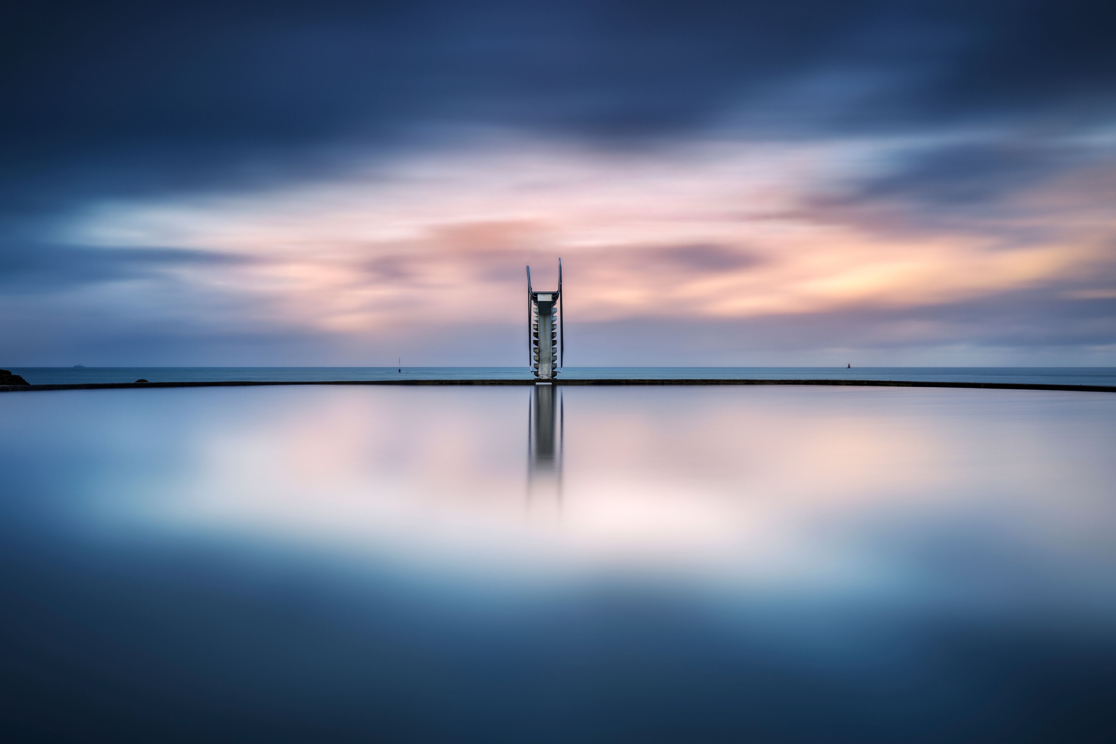A calm sea with a pier extending into it, under a twilight sky.