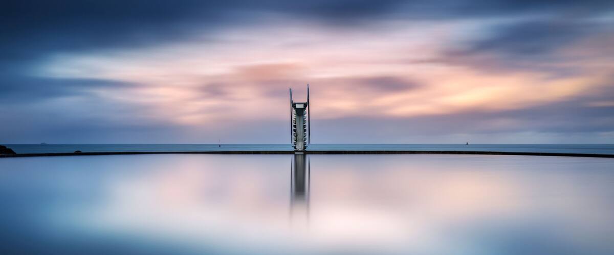 A calm sea with a pier extending into it, under a twilight sky.